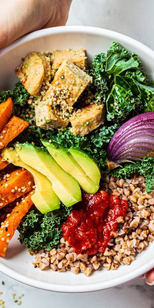 Baked vegetables, avocado, tofu and buckwheat buddha bowl. Vegan lunch salad with kale, baked sweet potato, tofu, buckwheat and avocado in a white bowl. Vegan concept.